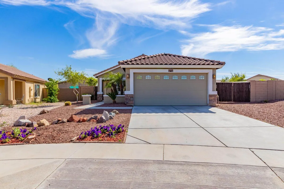 A welcoming exterior shot of the retreat, highlighting a tidy front porch, blooming flower beds, and a spacious driveway leading to the garage. The ambiance is inviting, ideal for gatherings or relaxing evenings under the desert sky.