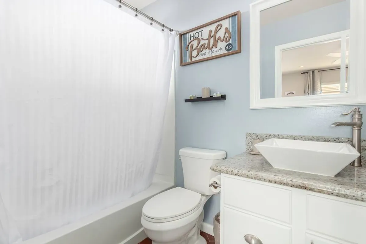 A serene, modern bathroom with a white bathtub behind a curtain, granite countertops, a decorative sign, and a sleek sink with a modern faucet. The space feels clean, spacious, and perfect for relaxation or self-care.