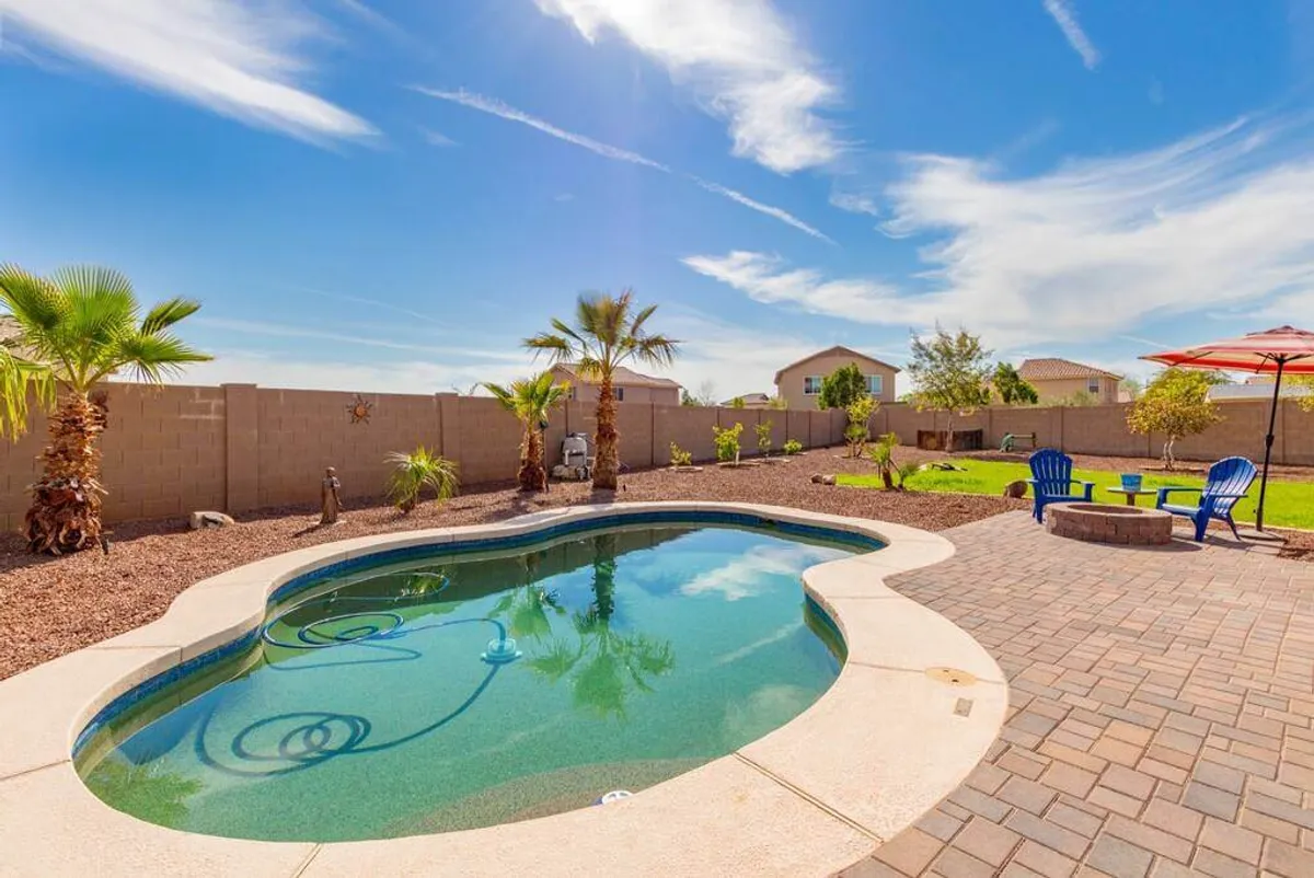 A pristine swimming pool is bordered by tall palm trees and several lounge chairs. A fire pit and umbrella-covered seating area create inviting spots for sunbathing, outdoor dining, and evening gatherings under the stars.