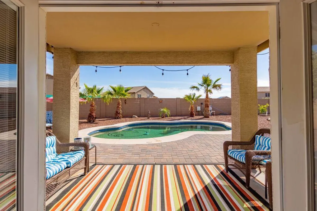 A relaxed, stylish pool area featuring palm trees, a striped outdoor rug, and comfortable outdoor seating. The space is designed for swimming, sunbathing, and casual socializing, with a tranquil vibe enhanced by the surrounding greenery.