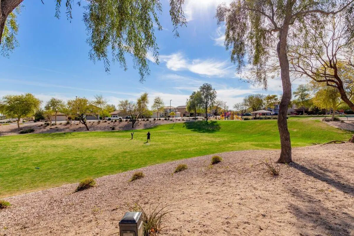 A lush green lawn stretches out with a playground visible in the background. People are seen enjoying the space—playing games, picnicking, and socializing, all in a relaxed outdoor environment.