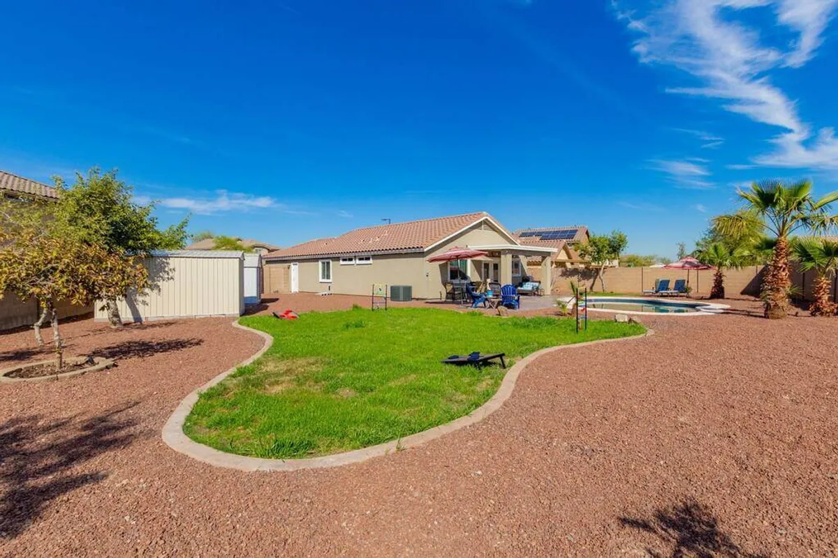 A vibrant exterior scene featuring a sparkling pool surrounded by green lawn, patio furniture, and tall palm trees. The setting is simultaneously inviting and serene, perfect for relaxing after a round of golf or enjoying an al fresco lunch under the palms.