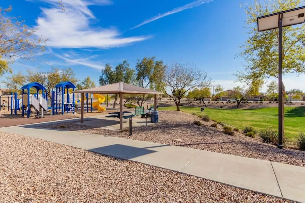 This image captures a vibrant community playground featuring colorful play equipment, a shaded picnic pavilion, and a wide open green space. Children and families can be seen enjoying the outdoors, hinting at the possibilities for group gatherings and playful afternoons.