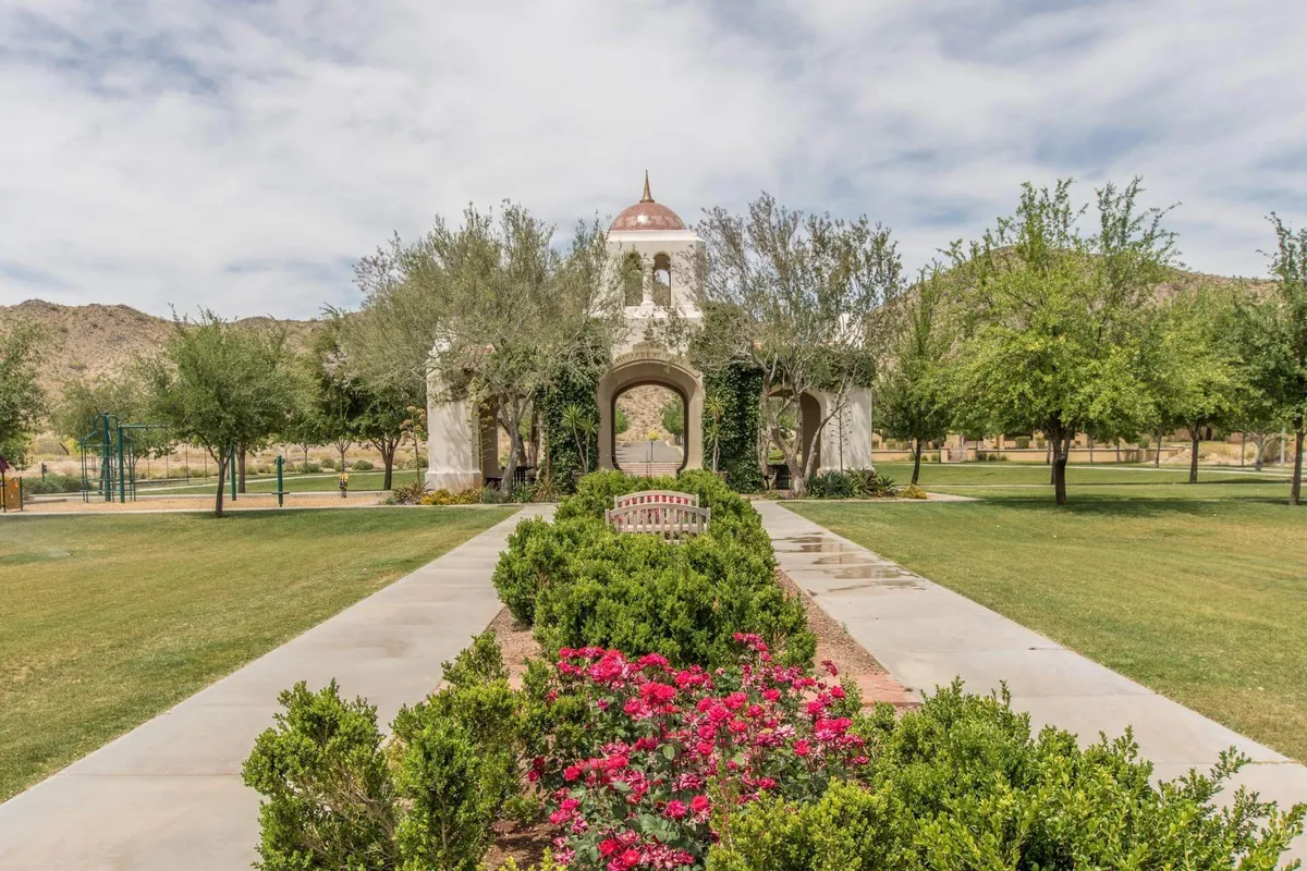 A tranquil exterior setting featuring an ornate domed structure surrounded by vibrant flower beds and a winding pathway. The scene is lush, peaceful, and showcases manicured landscaping perfect for quiet walks or moments of relaxation.
