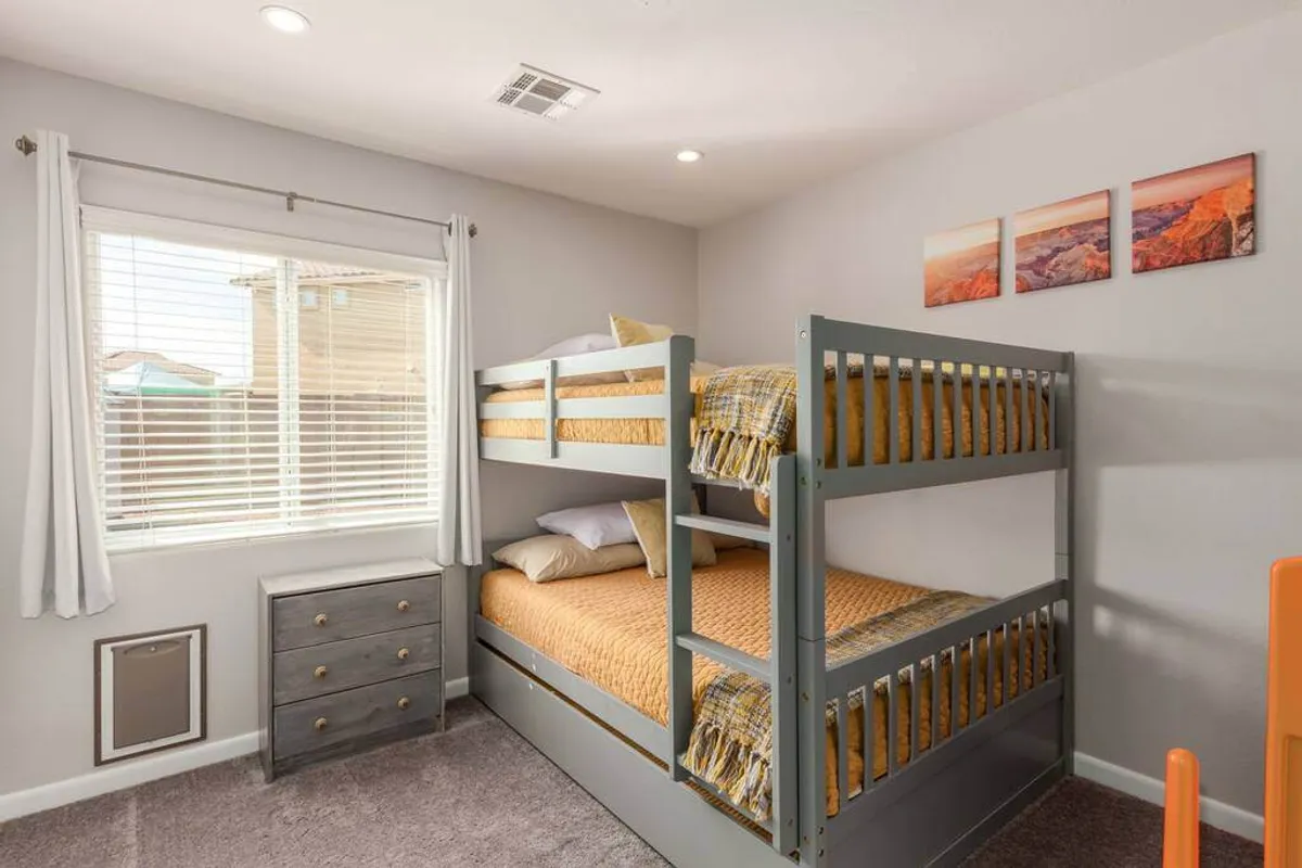 A playful and comfortable bedroom featuring a cozy bunk bed, window with natural light, dresser, and playful wall art. The room evokes a sense of fun and comfort, suitable for kids or guests.
