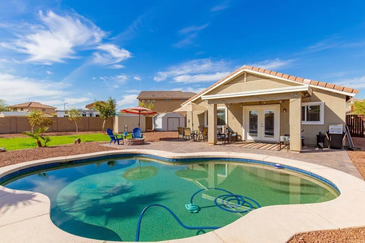 A cheerful backyard scene with a sparkling swimming pool, comfortable outdoor seating, a covered patio, and lush landscaping. The area is ideal for socializing, barbecuing, or enjoying quiet moments in the sun.