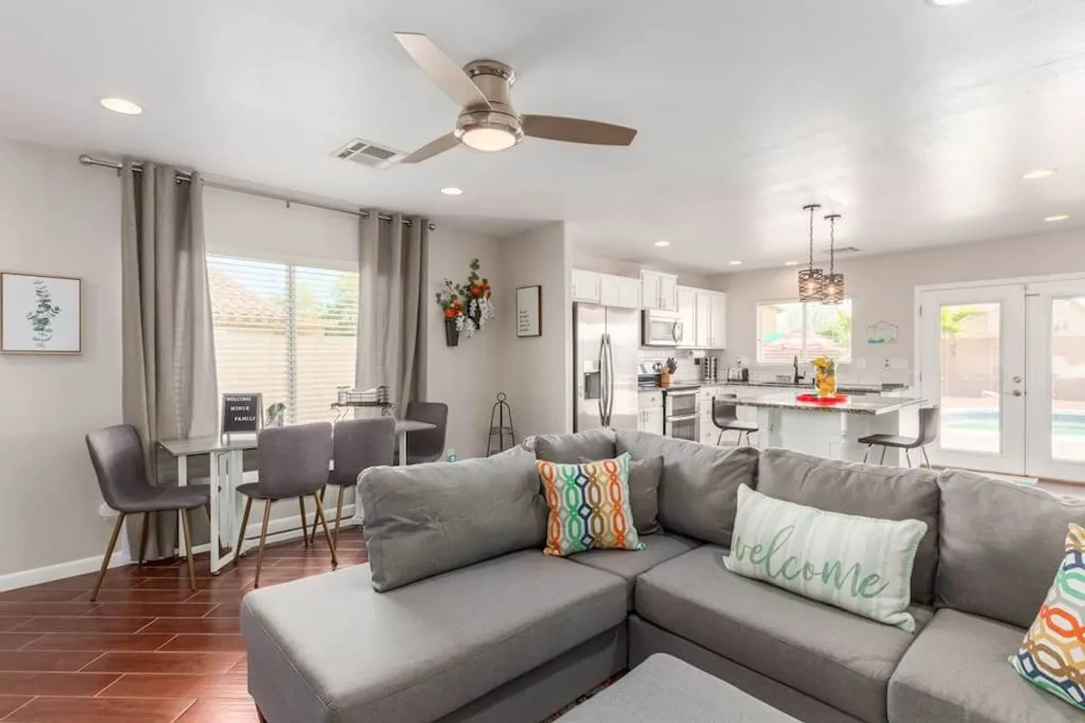 This image showcases a spacious open-concept interior featuring a large sectional sofa, a dining area, and a kitchen island. The décor incorporates warm tones and Southwestern accents, and the space is filled with natural light, creating a welcoming atmosphere ideal for gatherings and relaxation.